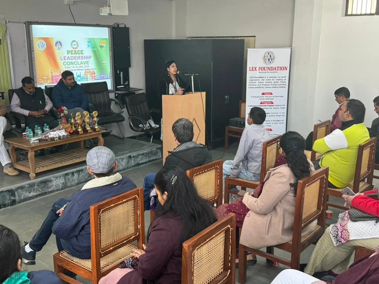 A speaker addressing an audience at a leadership conclave, with a Lex Foundation banner beside the podium.