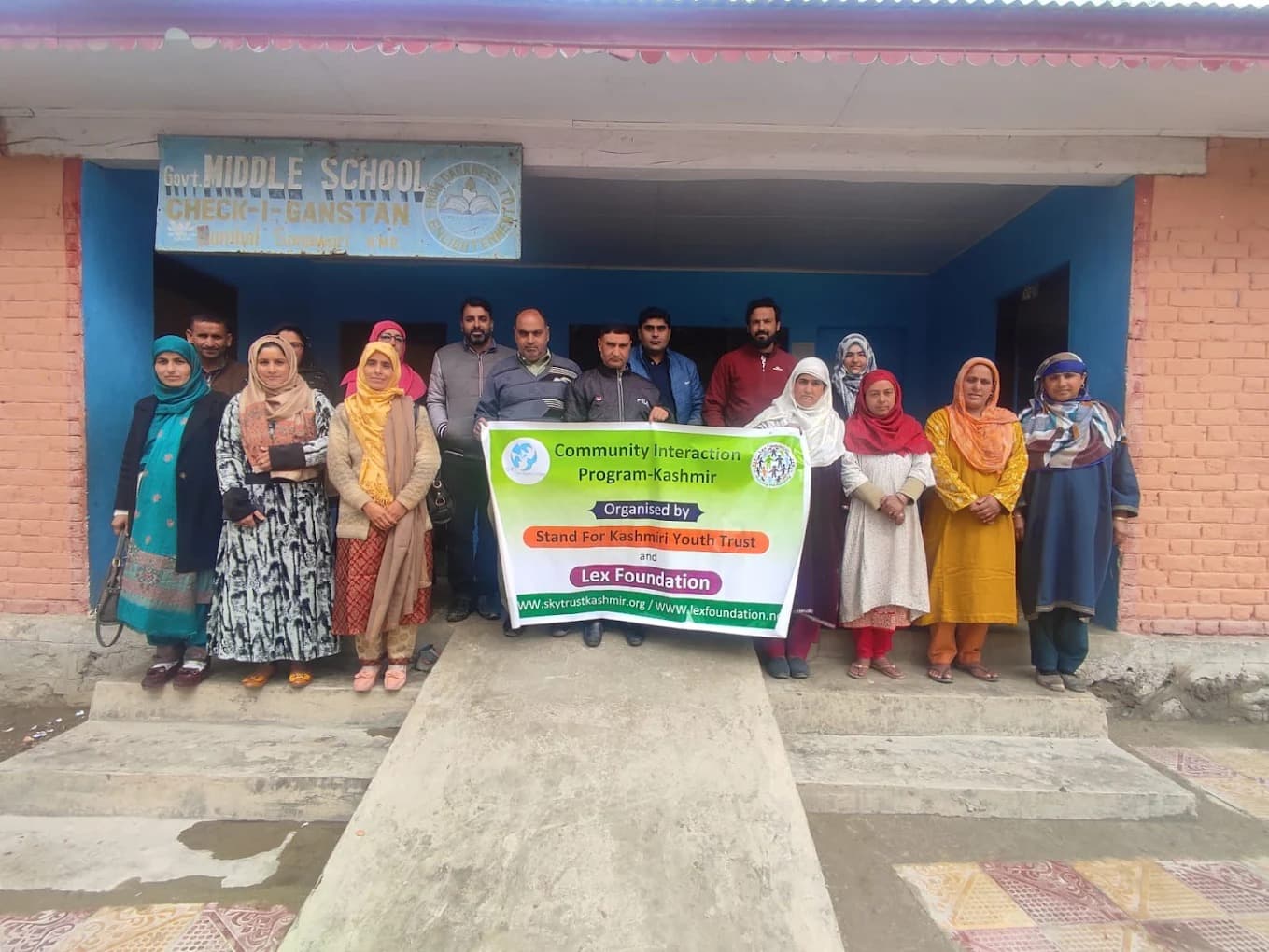 Group photograph outside a government middle school in Kashmir, holding a Community Interaction Programme banner.