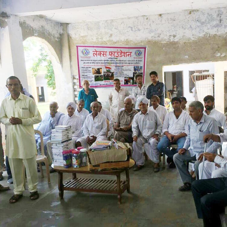 A group of elderly men seated at a community gathering beneath a Lex Foundation banner.