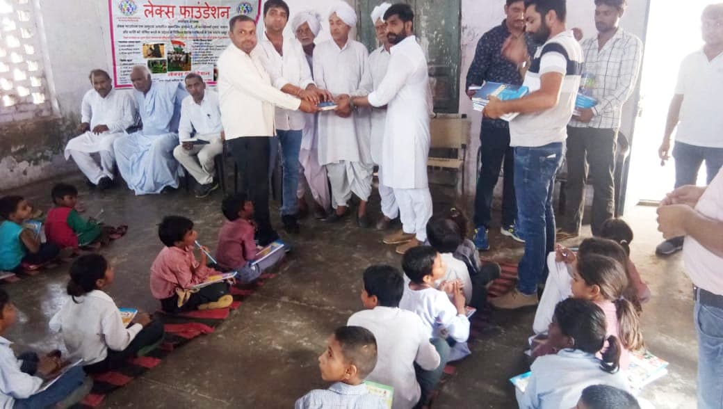 Children seated on the floor of a community hall receiving books from Lex Foundation volunteers.