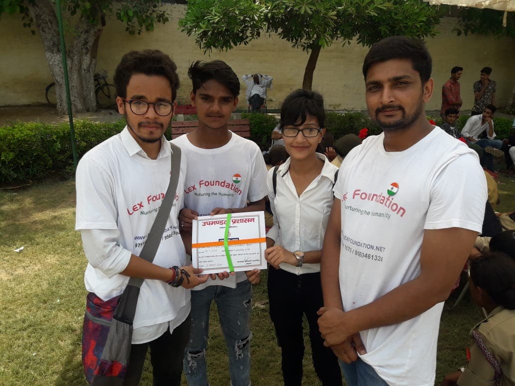 Lex Foundation volunteers presenting a certificate to community members outdoors, gathered under a tree.
